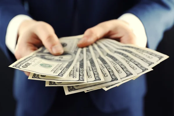 Businessman giving money on dark background — Stock Photo, Image