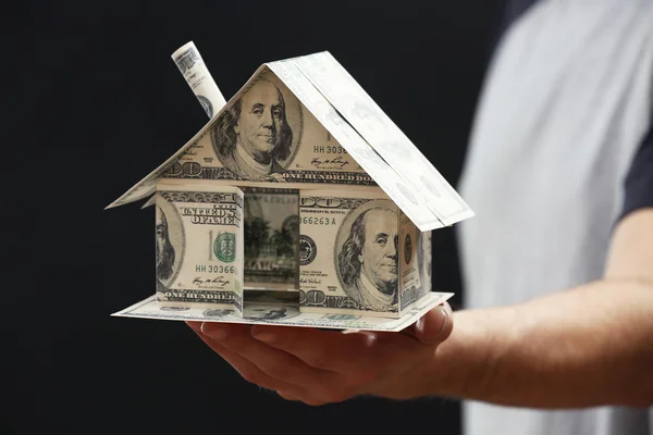 Model of house made of money in male hands on dark background — Stock Photo, Image