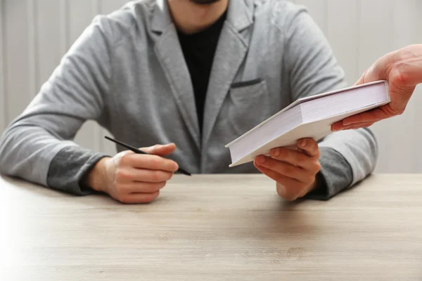 Author signing autograph in own book at wooden table on white planks background