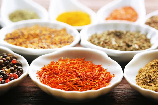 Different kinds of spices in ceramics spoons, close-up, on wooden background — Stock Photo, Image