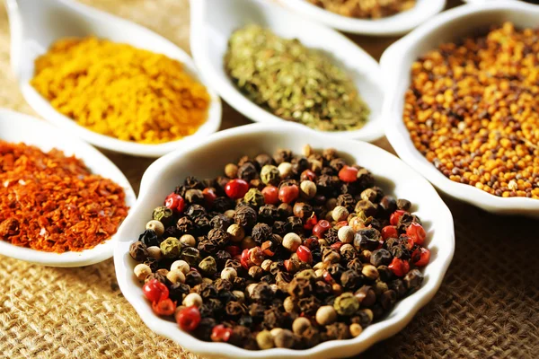 Different kinds of spices in ceramics spoons, close-up, on sackcloth background — Stock Photo, Image