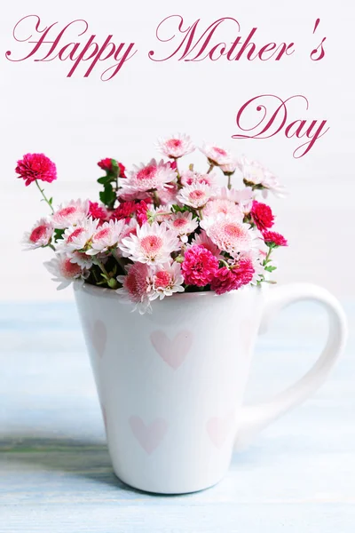 Beautiful flowers in cup on table on light background, Mother's Day concept — Stock Photo, Image