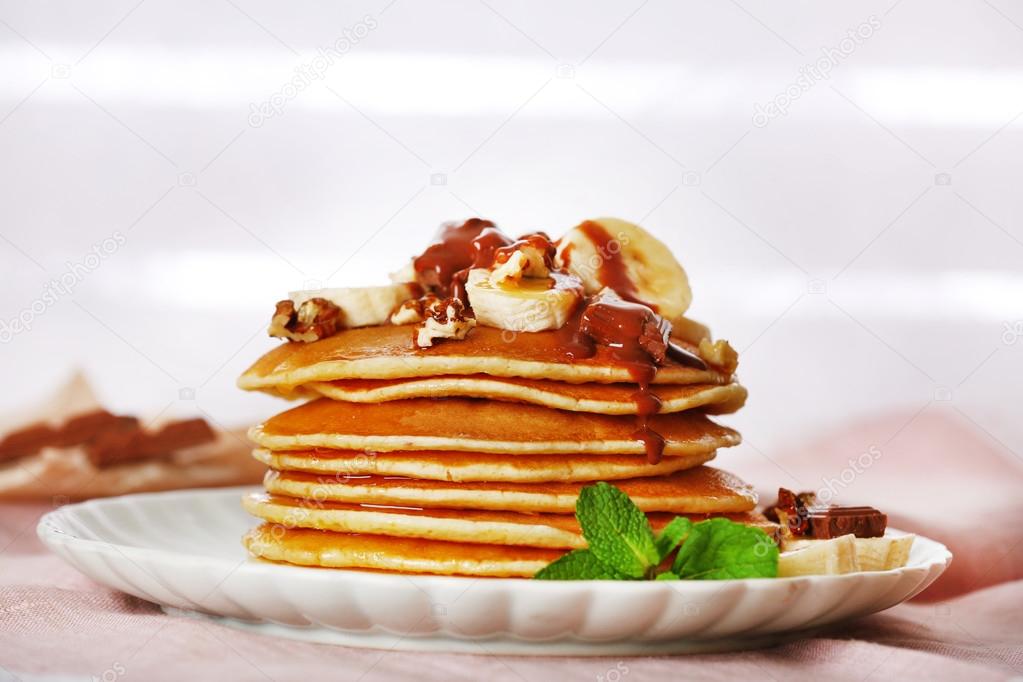 Stack of pancakes with mint, walnuts, chocolate and slices of banana on table with fabric on wooden planks background