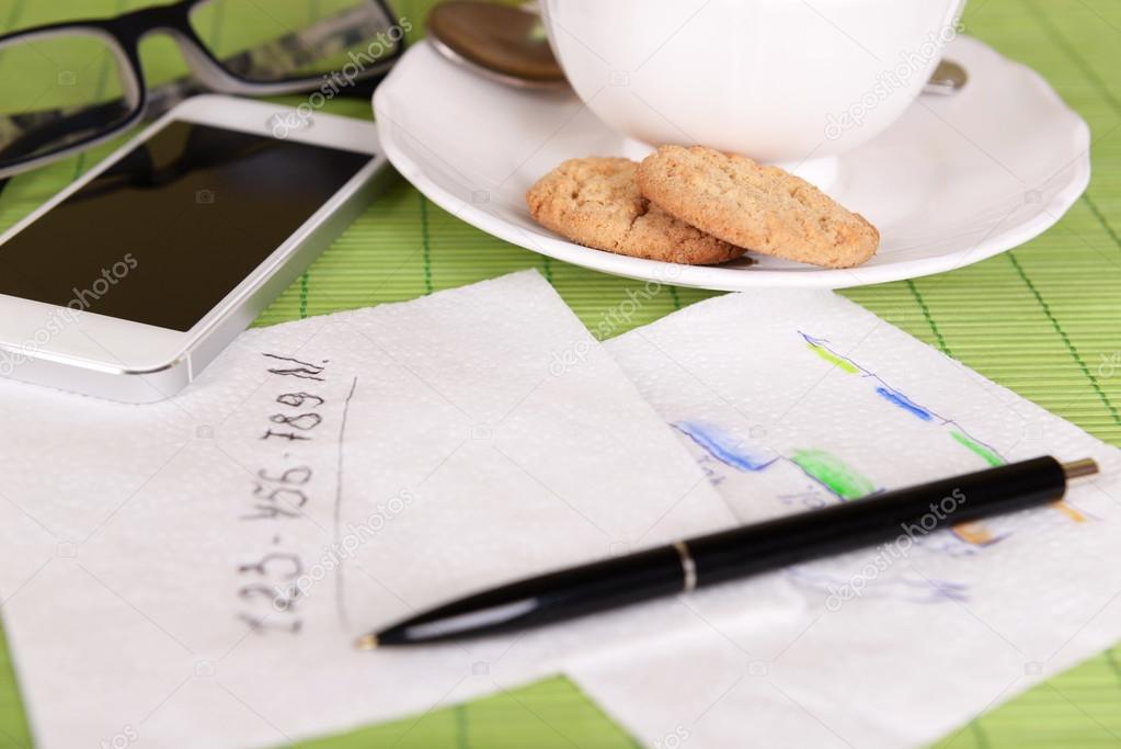 Cup of coffee with pen and business notes on napkin on green bamboo mat background