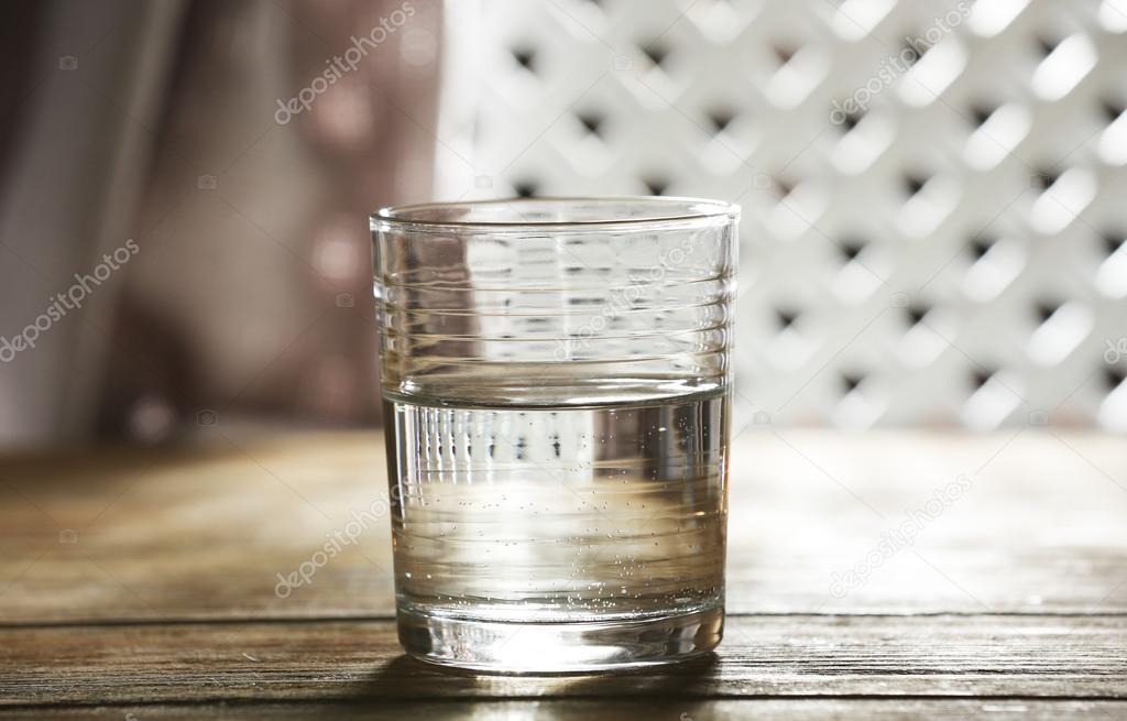 Glass of clean mineral water on wooden surface and lattice background