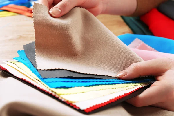 Échantillons de tissu coloré dans les mains féminines sur fond de table en bois — Photo