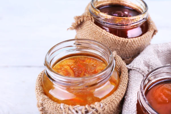 Pots faits maison de confiture de fruits dans des pochettes en toile de jute sur fond de planches de bois de couleur — Photo