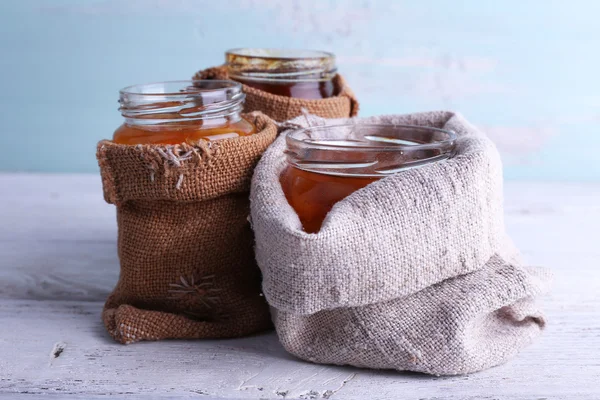 Pots faits maison de confiture de fruits dans des pochettes en toile de jute sur fond de table en bois et de mur de couleur — Photo