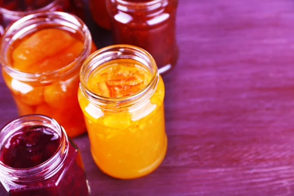 Frascos caseros de mermelada de frutas sobre fondo de madera de color — Foto de Stock