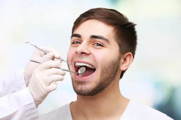 Examine of young man by dentist on light blurred background — Stock Photo, Image