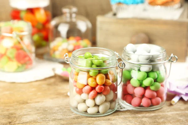 Multicolor snoepjes in glazen potten op houten achtergrond — Stockfoto