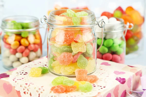 Vícebarevná cukroví ve sklenicích na barevné pozadí — Stock fotografie