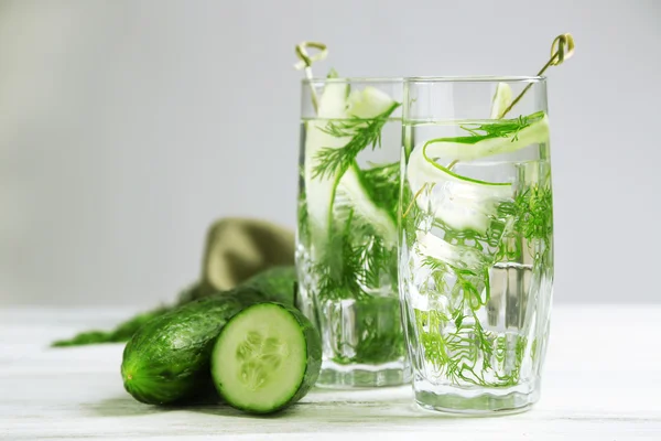 Gläser mit frischem Bio-Gurkenwasser auf Holztisch, auf grauem Hintergrund — Stockfoto