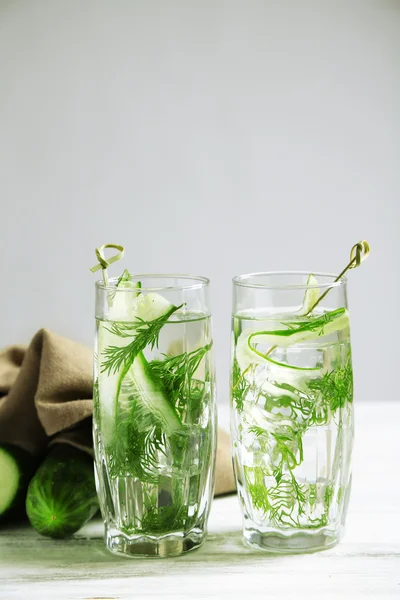 Gläser mit frischem Bio-Gurkenwasser auf Holztisch, auf grauem Hintergrund — Stockfoto