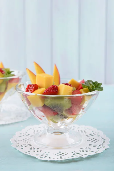 Fruitsalade met muntblaadjes in glaswerk op houten tafel en planken achtergrond — Stockfoto