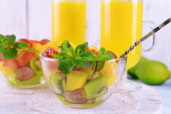水果沙拉配薄荷和彩色木制背景上的玻璃器皿中的橙汁 — 图库照片