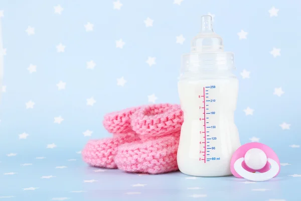 Babymilchflasche, Schnuller und Babystiefel auf blauem Hintergrund — Stockfoto