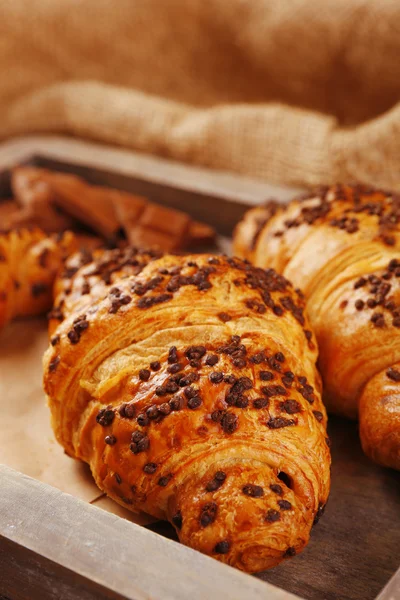 Croissant freschi e gustosi con cioccolato su vassoio di legno, su fondo sacco — Foto Stock