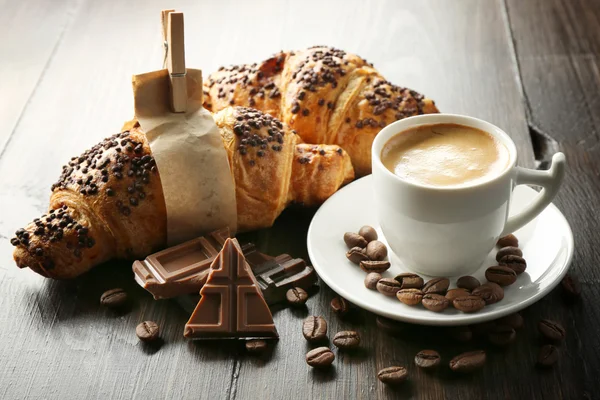 Frische und leckere Croissants mit Schokolade und Tasse Kaffee auf Holzgrund — Stockfoto