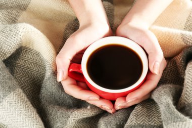 Cup of coffee in hands on plaid background