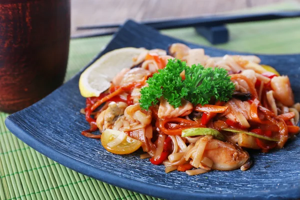 Fideos chinos con verduras y mariscos en plato sobre fondo de estera de bambú —  Fotos de Stock