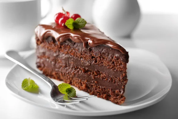 Köstlicher Schokoladenkuchen auf Teller auf Tisch vor hellem Hintergrund — Stockfoto