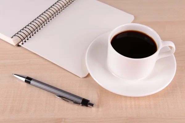 Šálek kávy na talířek s Poznámkový blok a pero na dřevěný stůl pozadí — Stock fotografie