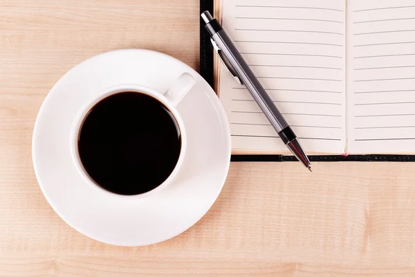 Tazza di caffè su piattino con diario e penna su sfondo tavolo in legno — Foto Stock