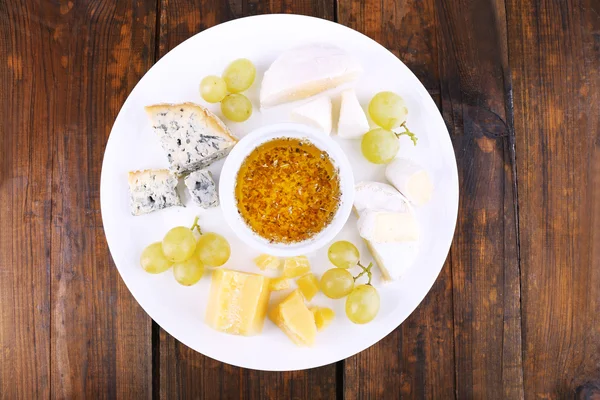 Διαφορετικό είδος τυριού με σταφύλι και πιατάκι στο πιάτο σε ξύλινο τραπέζι φόντο — Φωτογραφία Αρχείου