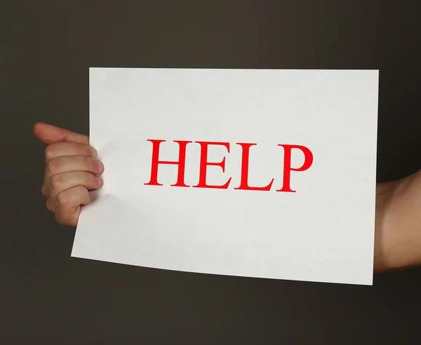 Sheet of paper with Help sign in male hand on dark background — Stock Photo, Image