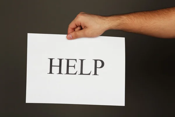 Sheet of paper with Help sign in male hand on dark background — Stock Photo, Image