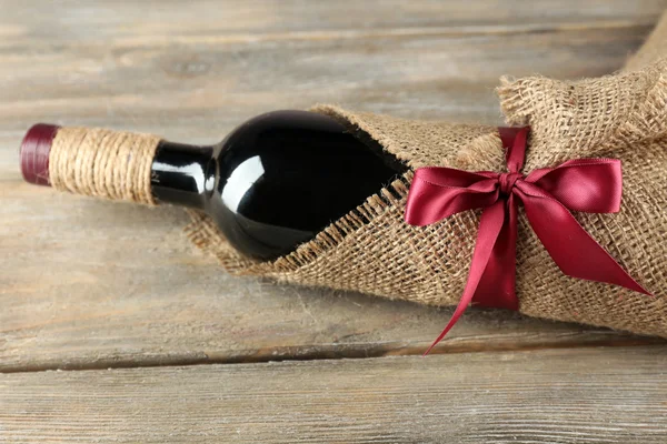 Botella de vino tinto envuelta en tela de arpillera sobre tablones de madera —  Fotos de Stock