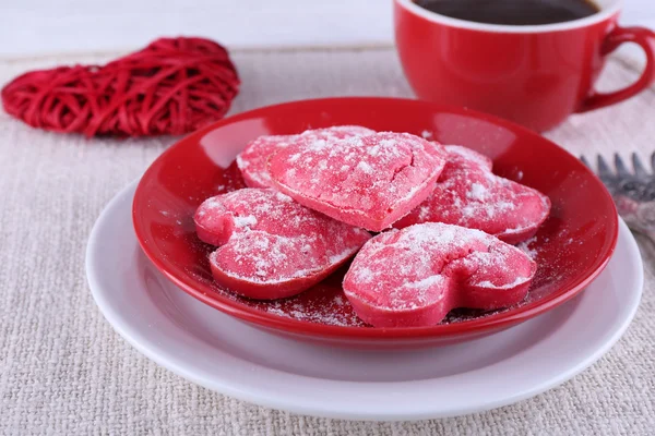 Cookies in vorm van hart op plaat met kop koffie op servet en kleur houten planken achtergrond — Stockfoto