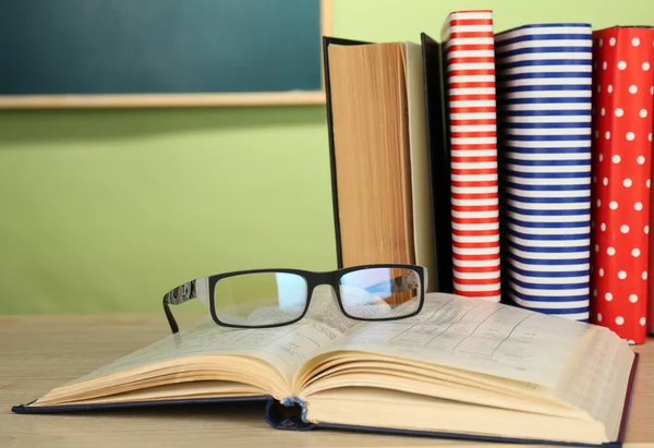 Handboeken met een bril op houten bureau, op kleurrijke muur en schoolbord achtergrond — Stockfoto