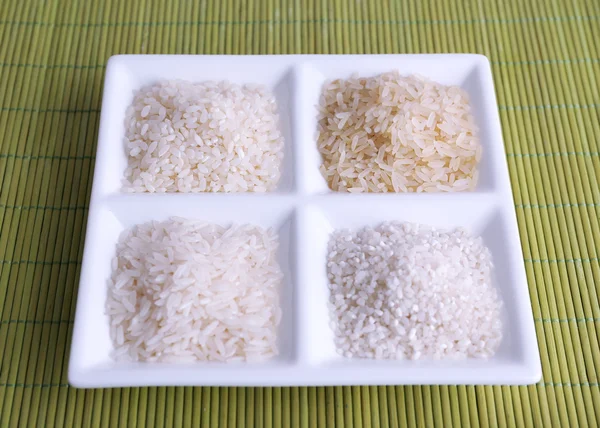 Different types of rice on plate on bamboo background — Stock Photo, Image