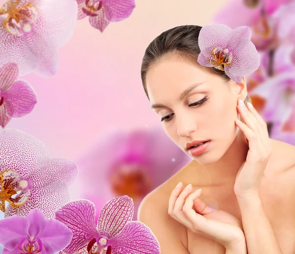 Hermosa mujer joven con flor de orquídea en el pelo sobre fondo de flores de orquídea rosa —  Fotos de Stock