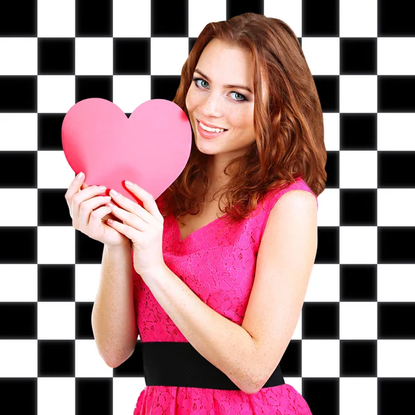 Beautiful young girl with heart in hands on checkered background — Stock Photo, Image