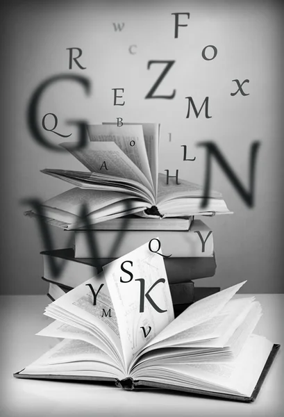 Muitos livros com letras voadoras na mesa sobre fundo escuro — Fotografia de Stock