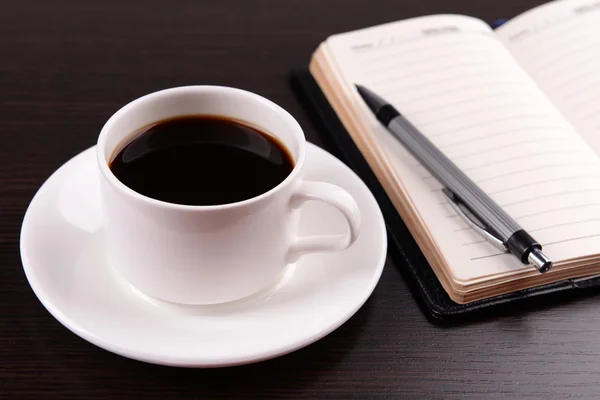 Tazza di caffè su piattino con diario e penna su sfondo tavolo in legno — Foto Stock