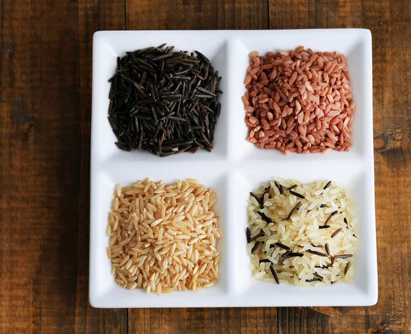 Diferentes tipos de arroz en plato sobre fondo de madera — Foto de Stock