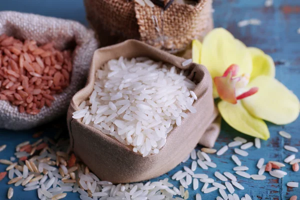 Diferentes tipos de arroz em sacos no fundo de madeira — Fotografia de Stock