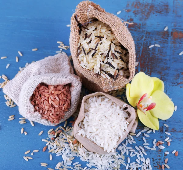 Diferentes tipos de arroz en sacos sobre fondo de madera — Foto de Stock