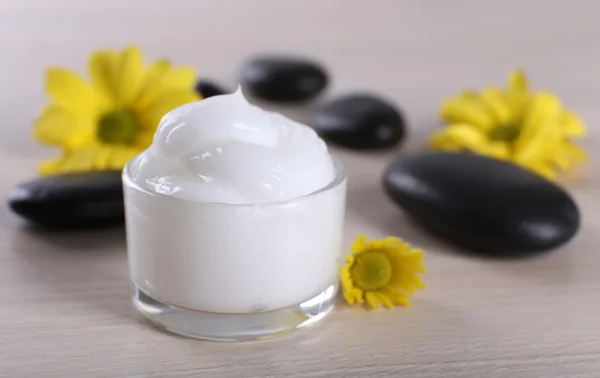 Creme cosmético com flores e pedras de spa em fundo de madeira — Fotografia de Stock