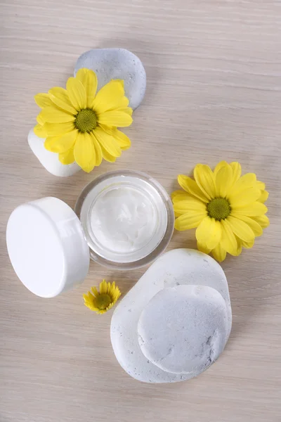 Crema cosmética con flores y piedras de spa sobre fondo de madera —  Fotos de Stock