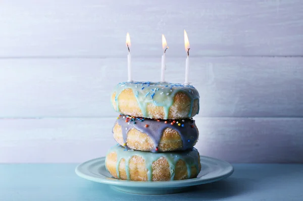 Délicieux beignets avec glaçage et bougies d'anniversaire sur la table sur fond en bois — Photo