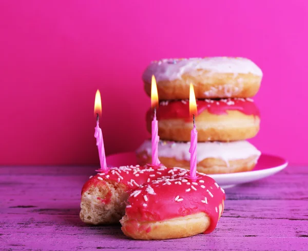 Delicious donuts with icing and birthday candles on table on bright background — Stock Photo, Image