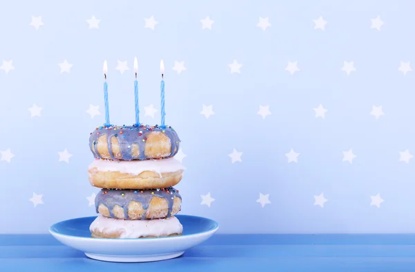 Deliciosos donuts com gelo e velas de aniversário na mesa em fundo brilhante — Fotografia de Stock