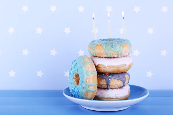 Deliciosos donuts com gelo e velas de aniversário na mesa em fundo brilhante — Fotografia de Stock