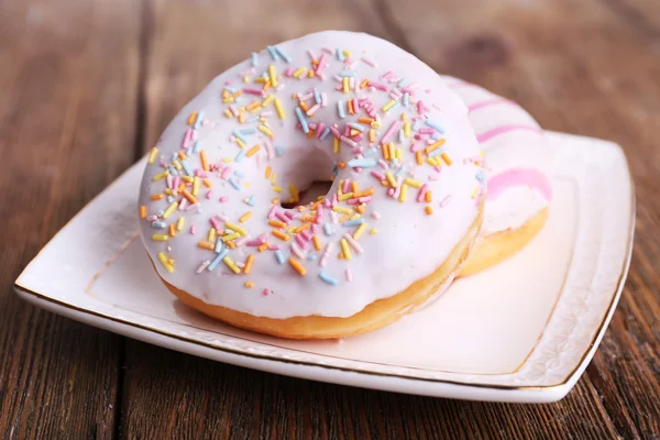 Deliciosos donuts com cobertura na placa em fundo de madeira — Fotografia de Stock