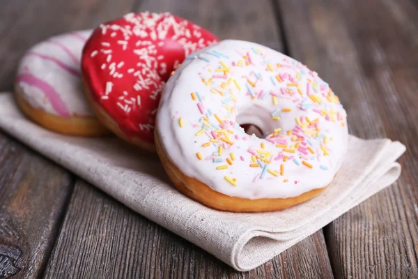 Köstliche Donuts mit Sahnehäubchen auf Serviette auf Holzgrund — Stockfoto